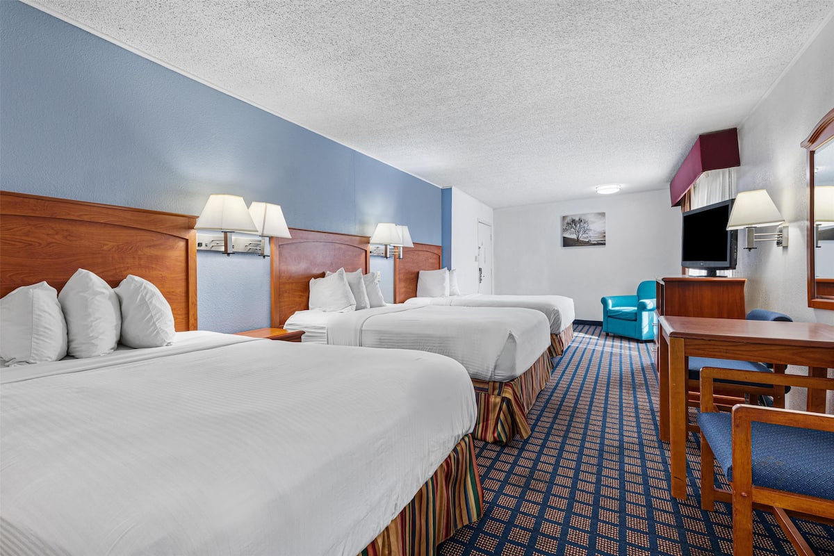 A hotel room with three beds, a desk, a chair, and a television.