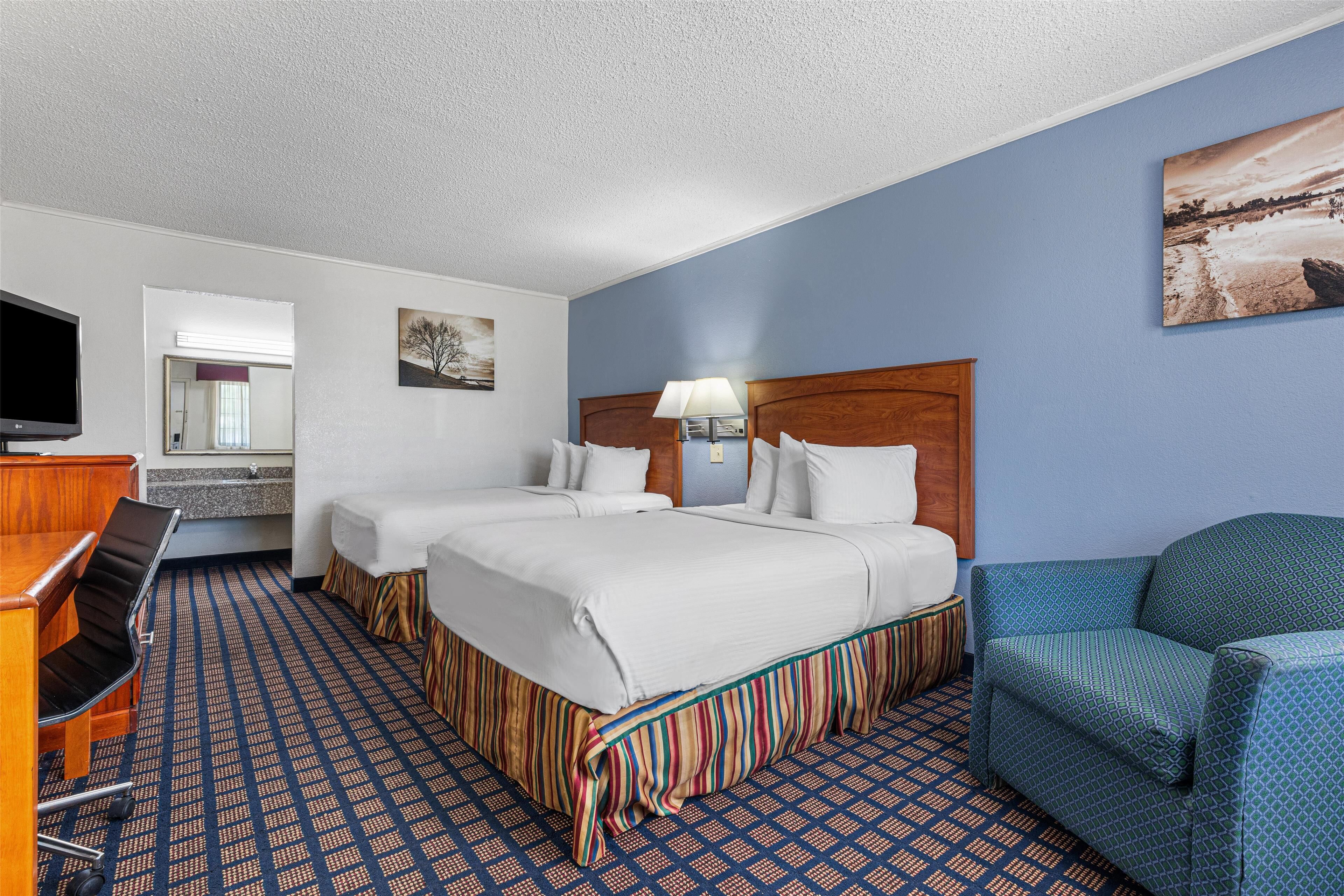 A hotel room with two beds, a desk with a chair, a TV, and a painting on the wall.
