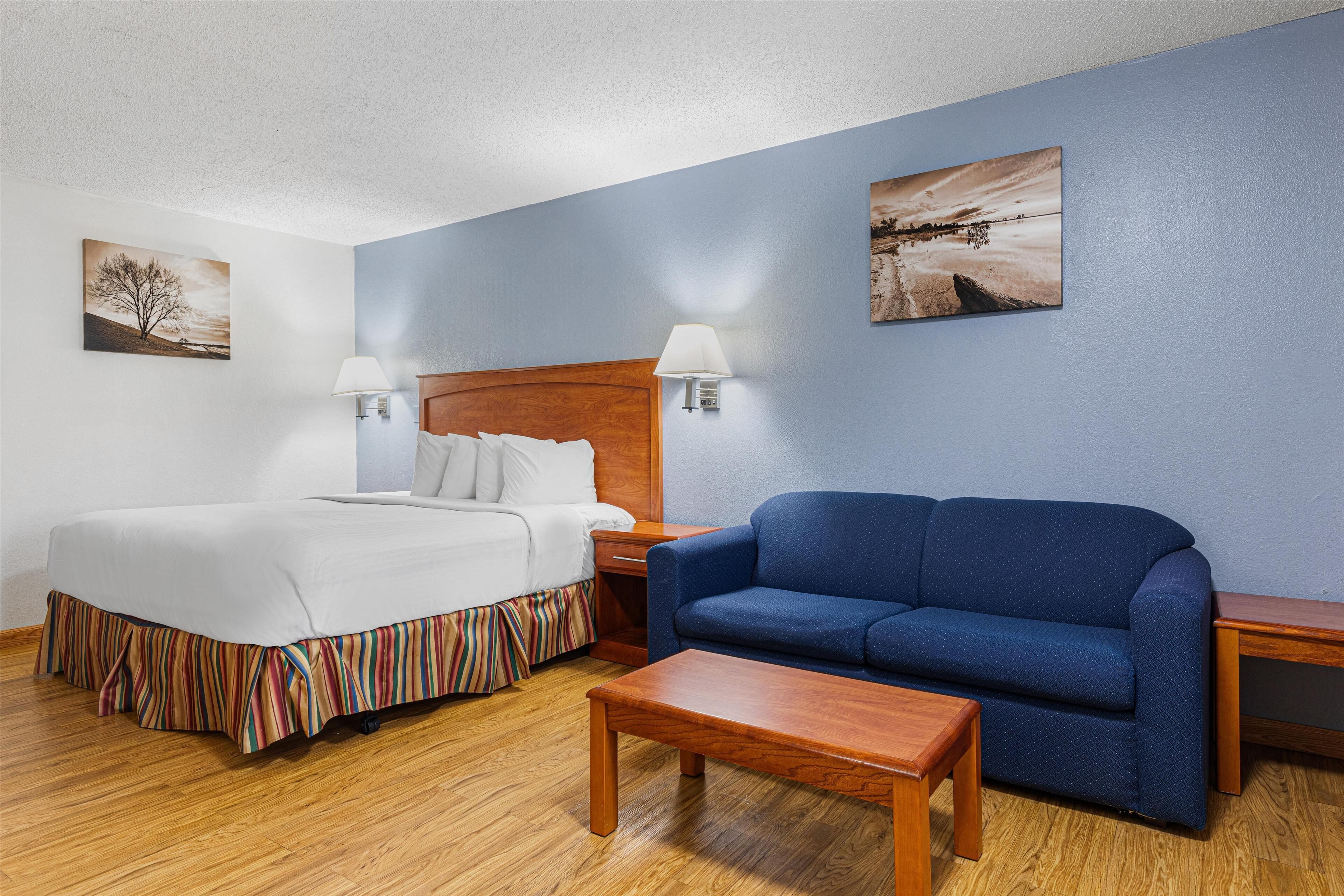 A hotel room with a bed, a blue sofa, a wooden coffee table, and two bedside tables with lamps.