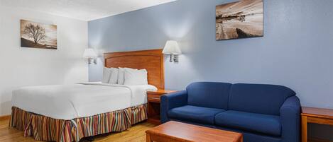A hotel room with a bed, a blue sofa, a wooden coffee table, and two bedside tables with lamps.
