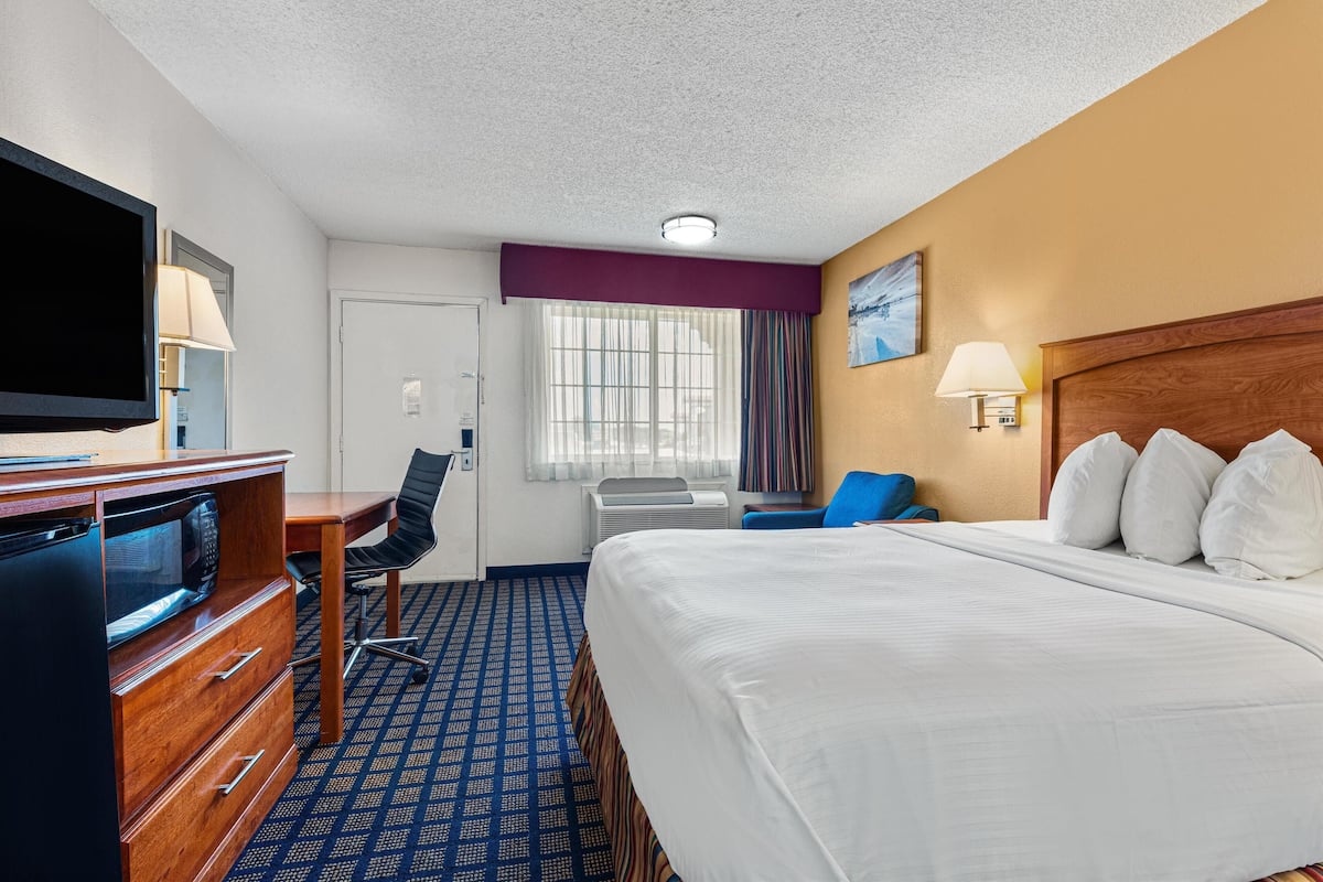 A hotel room with a large bed, a desk with a computer, a television, and a window with curtains.