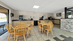 A modern kitchen with wooden dining tables and chairs, a refrigerator, and a coffee machine.