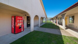 Un couloir avec un distributeur automatique de Coca-Cola, une allée couverte et un espace verdoyant.