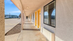 A long corridor with yellow doors and large windows, leading to a parking area.