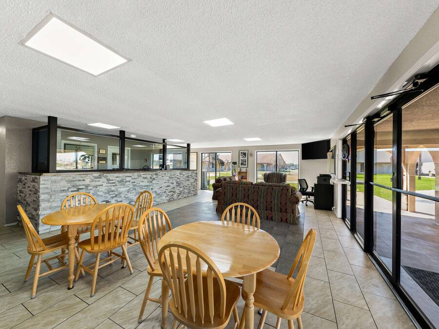 A spacious indoor area with a wooden dining table and chairs, a stone accent wall, and large windows offering views of the outdoors.