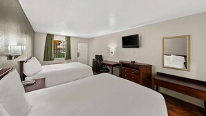 A hotel room with two beds, a desk, a chair, a TV, a mirror, and a window with curtains.