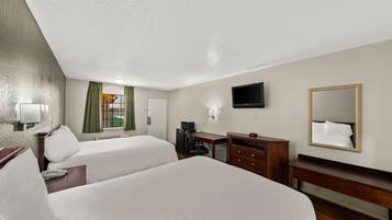 A hotel room with two beds, a desk, a chair, a TV, a mirror, and a window with curtains.