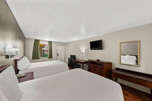 A hotel room with two beds, a desk, a chair, a TV, a mirror, and a window with curtains.