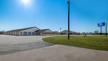 A commercial building with a parking lot, a grassy area, and a clear blue sky.
