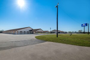 A commercial building with a parking lot, a grassy area, and a clear blue sky.