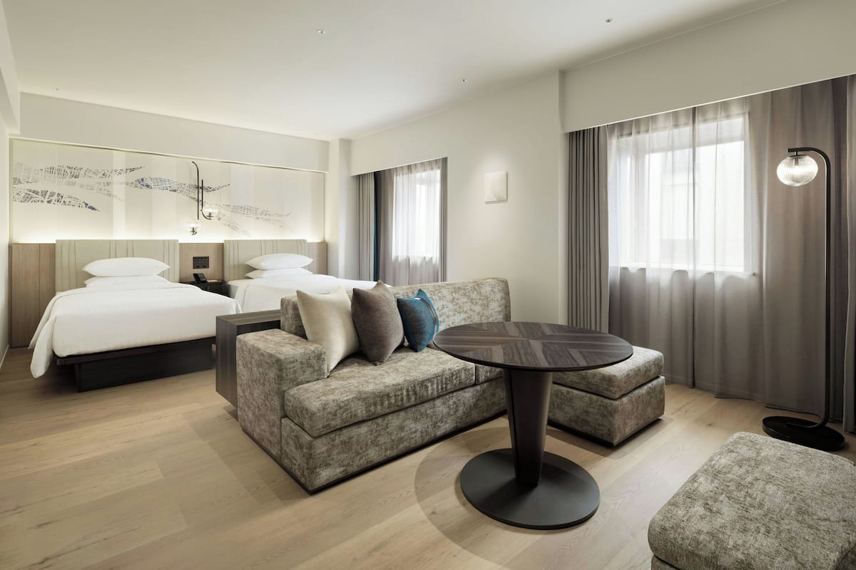 A modern hotel room with a bed, a sofa, a round table, and a large window with curtains.