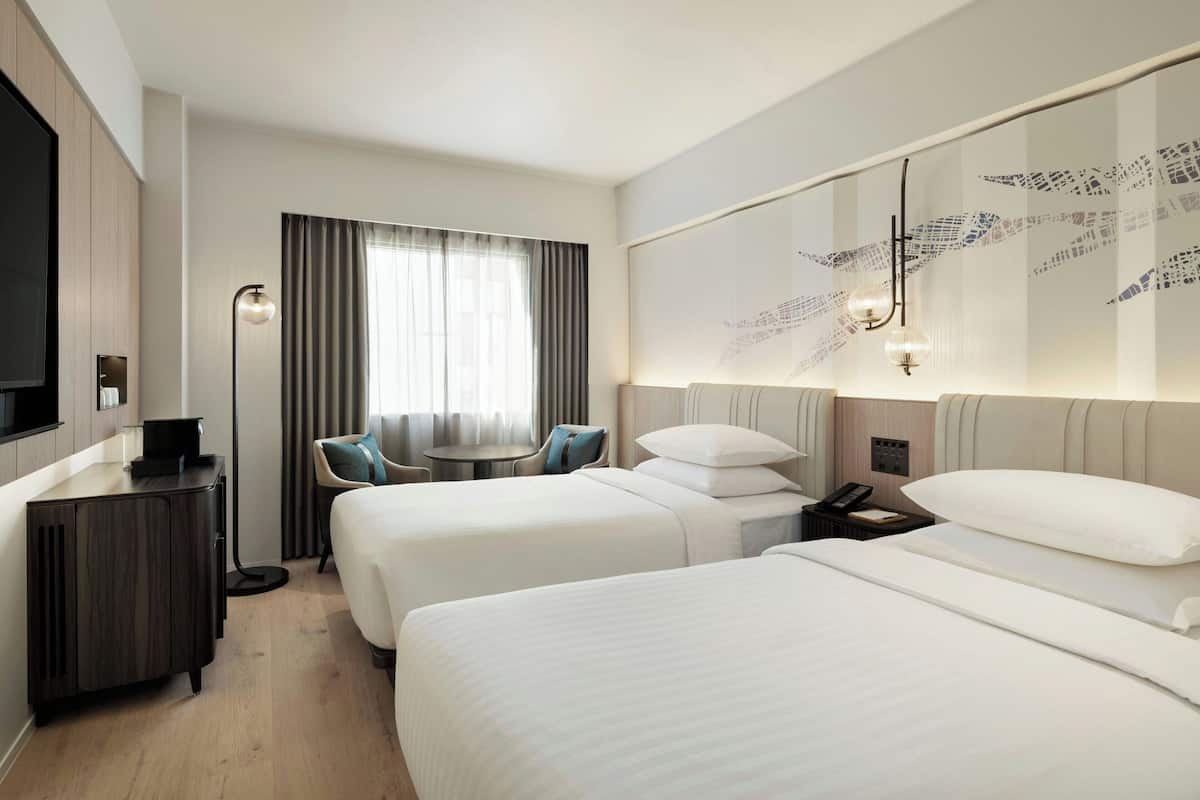 A hotel room with two beds, a desk, a chair, a TV, and a wall-mounted artwork.