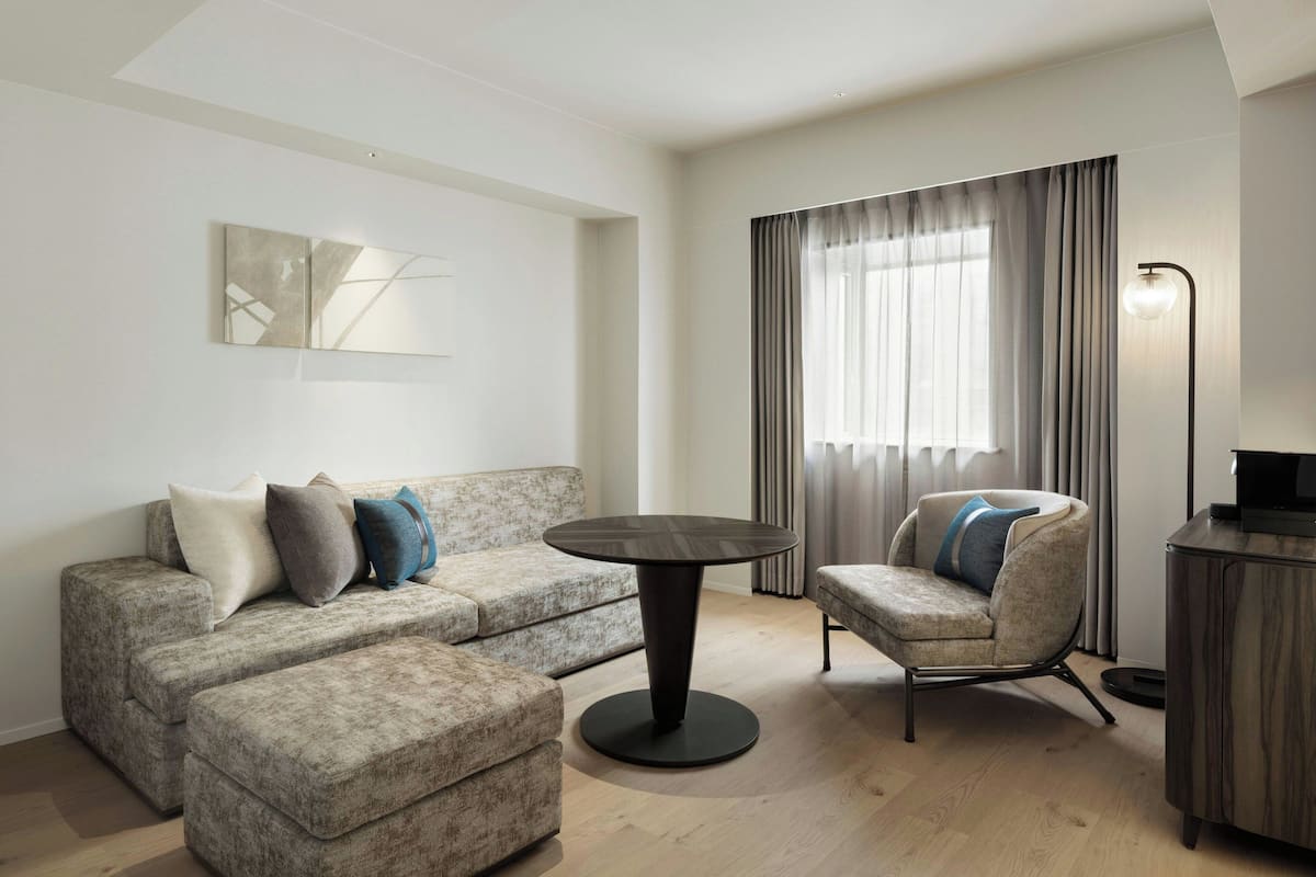 A modern living room with a grey sofa, a round coffee table, a grey armchair, and a dark wooden cabinet.
