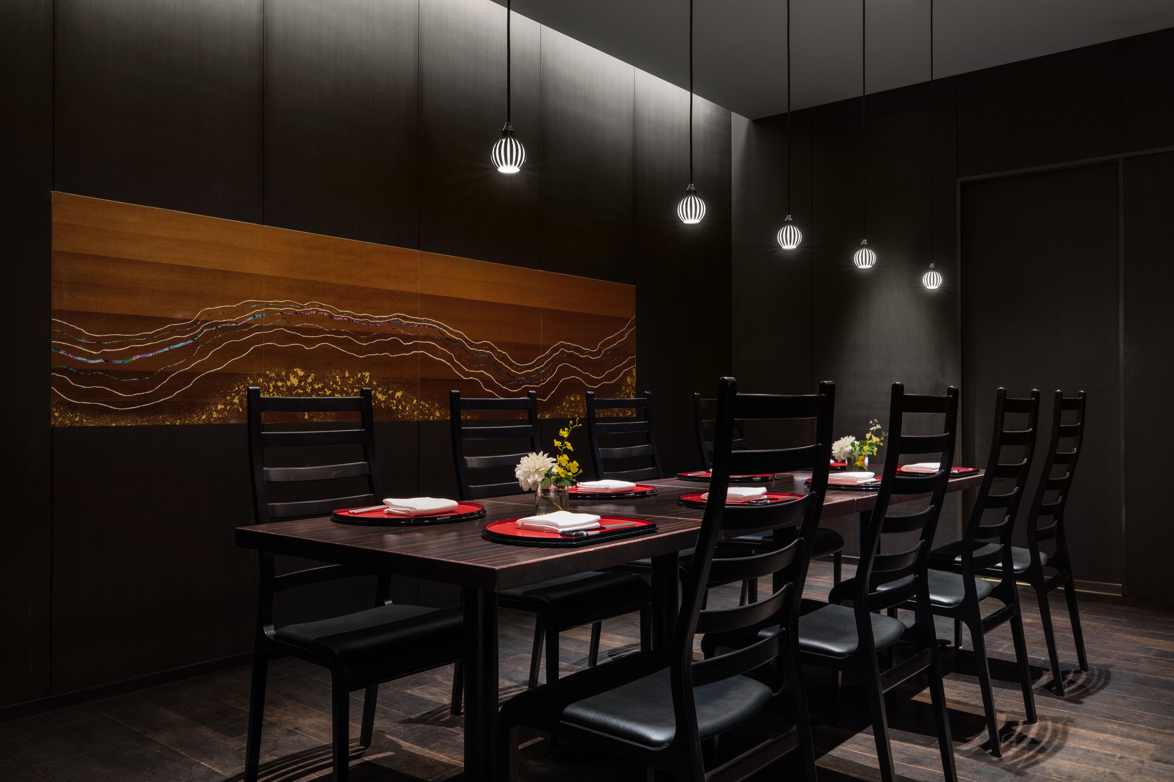 Un moderno comedor con una larga mesa dispuesta para varias personas, paredes de madera oscura y lámparas colgantes.