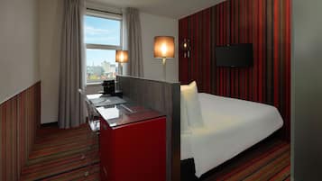 A hotel room with a bed, a desk, a chair, a TV, and a window with curtains.