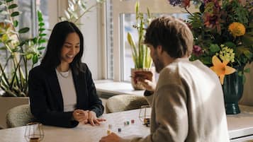 Twee personen zitten aan een tafel met dobbelstenen, wat aangeeft dat er een spel gespeeld wordt.