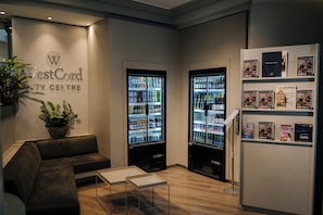Zona de recepción de WestCord City Centre con asientos, un refrigerador lleno de bebidas y un perchero con revistas.