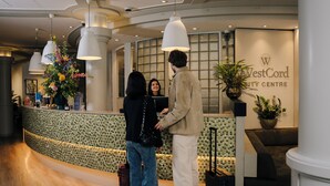 A reception area with a curved counter, a large potted plant, and a sign for WestCord City Centre. - WestCord City Centre Hotel Amsterdam (Amsterdam)