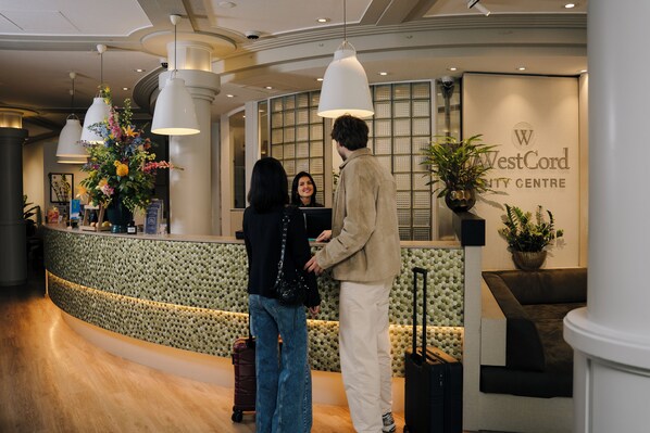 A reception area with a curved counter, a large potted plant, and a sign for WestCord City Centre.