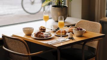 Una mesa de desayuno con croissants, un tazón de cereal, un vaso de jugo de naranja y un plato de fruta.