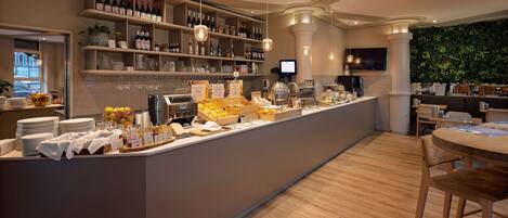 A modern bar area with a variety of bottles and glasses, a counter with food items, and a seating area with tables and chairs.