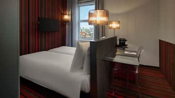 Een hotelkamer met een groot bed, een bureau met stoel, een aan de muur bevestigde televisie en een raam met uitzicht op de stad.