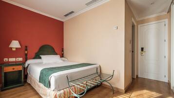 Una habitación de hotel con cama, mesita de noche, lámpara, radiador y puerta.