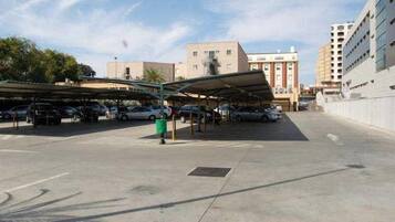 Un estacionamiento con espacios de aparcamiento techados y un contenedor verde para basura.