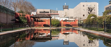 A hotel with a pool reflecting the building and trees.