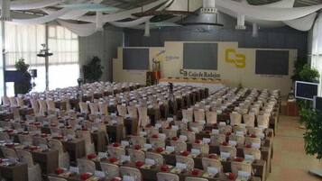 A conference room with rows of tables and chairs, a stage with a banner, and a large screen.