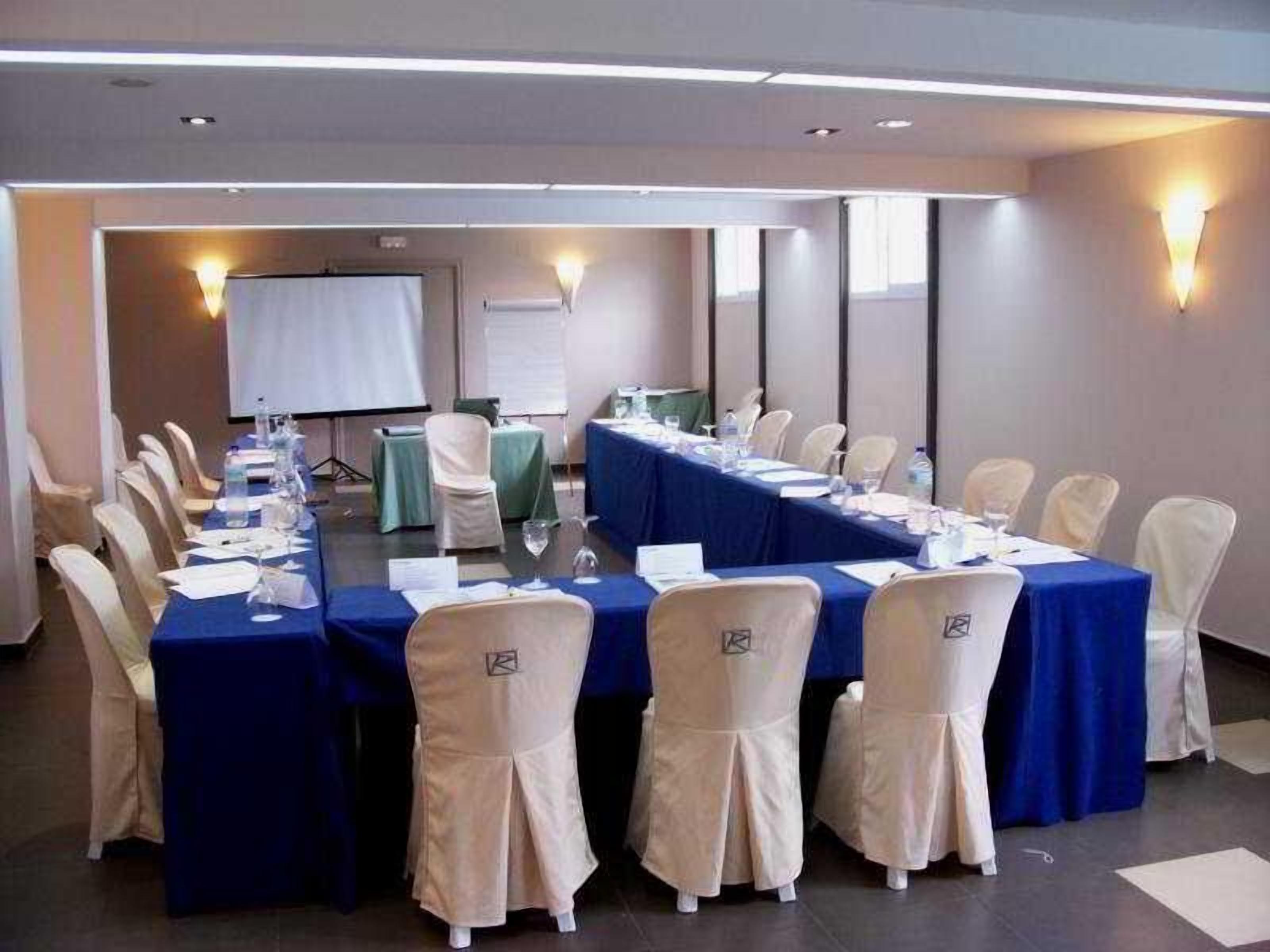 Ein Konferenzraum mit einem langen Tisch, Stühlen und einer Projektionsleinwand.