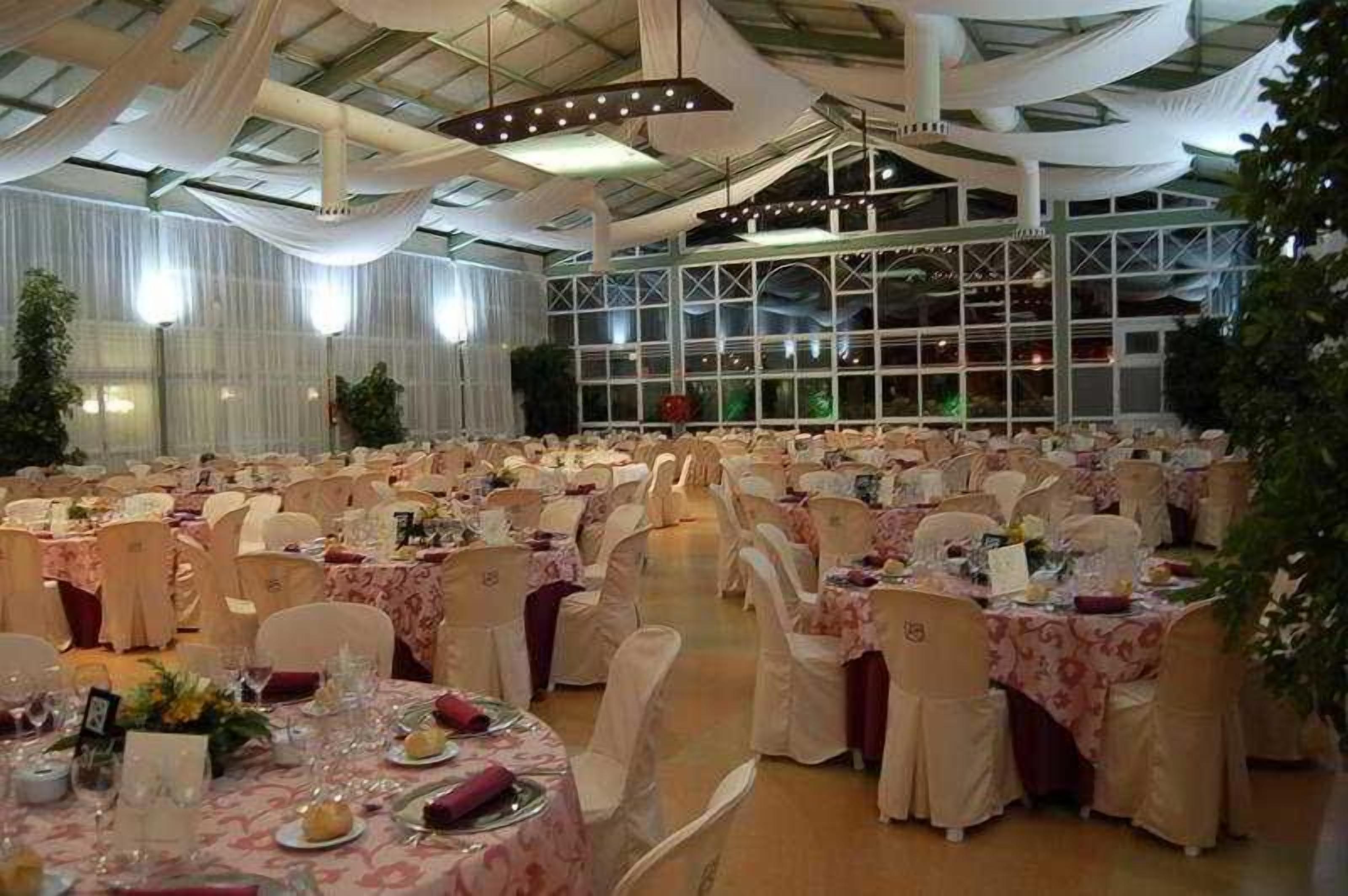 Une salle de banquet avec des tables rondes, des chaises blanches et des décorations suspendues au plafond.