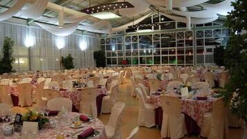Une salle de banquet avec des tables rondes, des chaises blanches et des décorations suspendues au plafond.