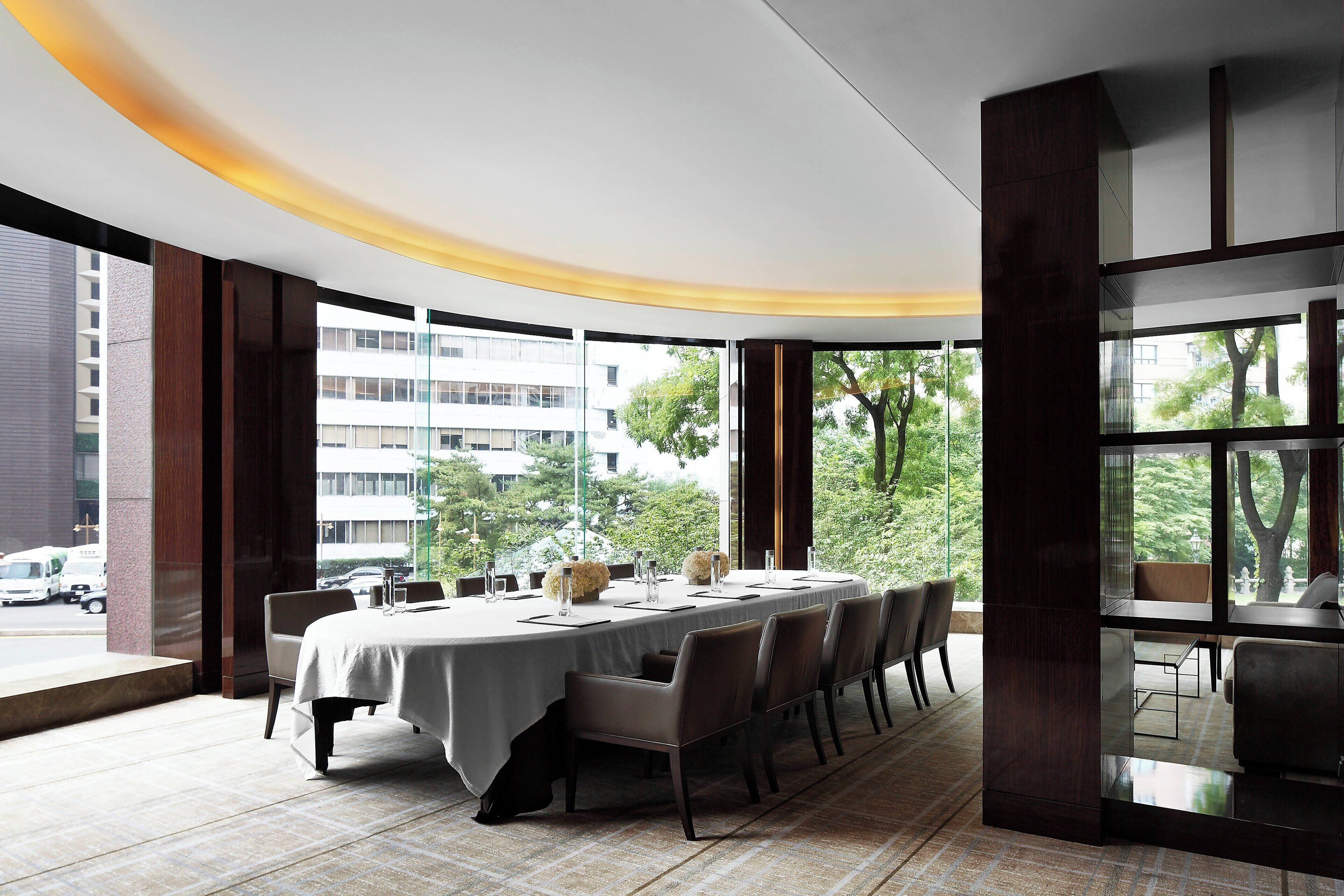 Un'area pranzo moderna con un tavolo lungo apparecchiato per sei persone, ampie finestre che offrono vista sulla città e un design del soffitto curvo.