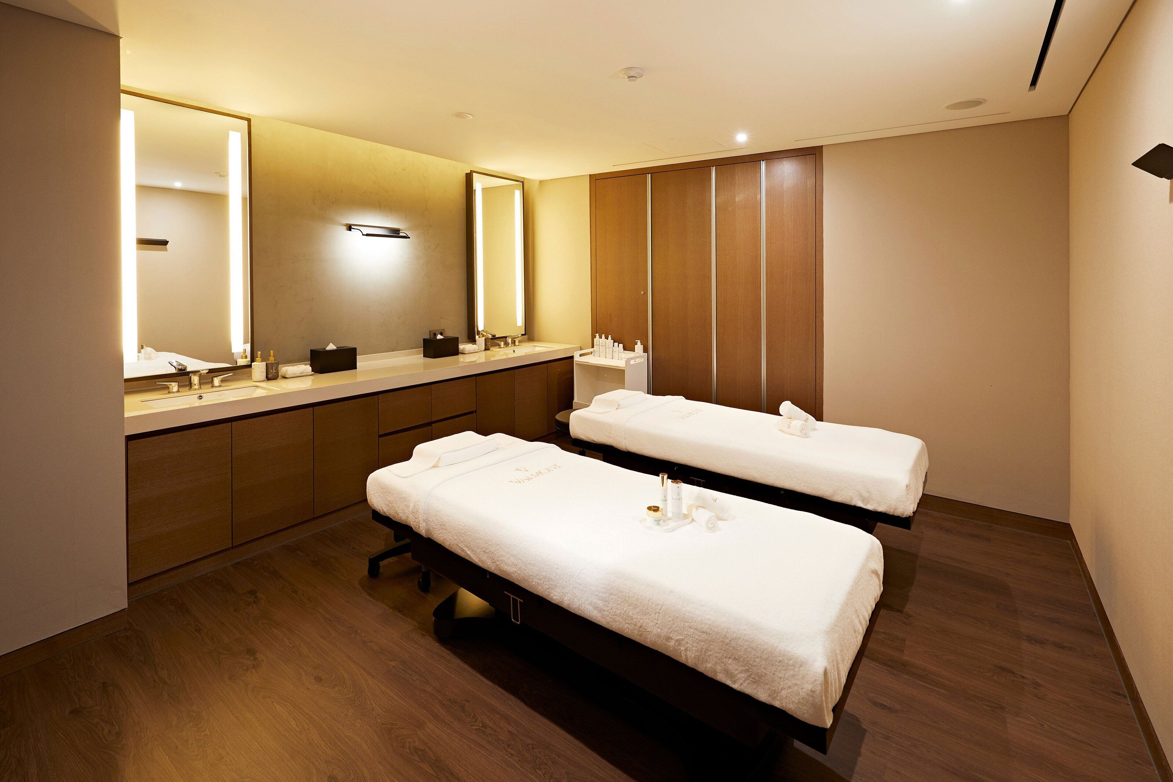 A modern bathroom with two beds, a large mirror, and wooden cabinets.