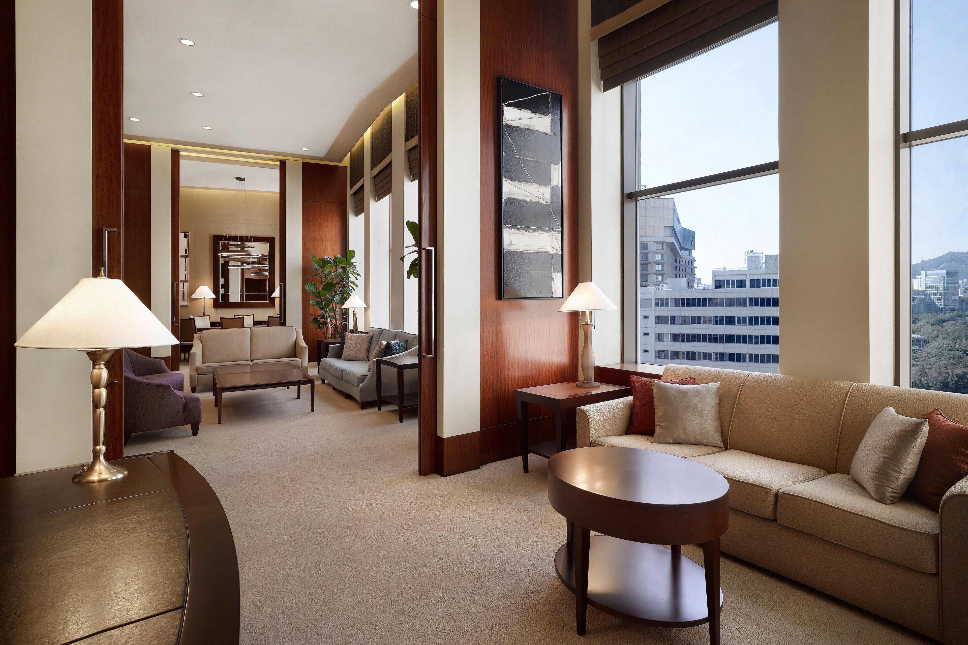 Un moderno vestíbulo de hotel con un sofá, sillones, una mesa de centro y un ventanal con vistas a la ciudad.