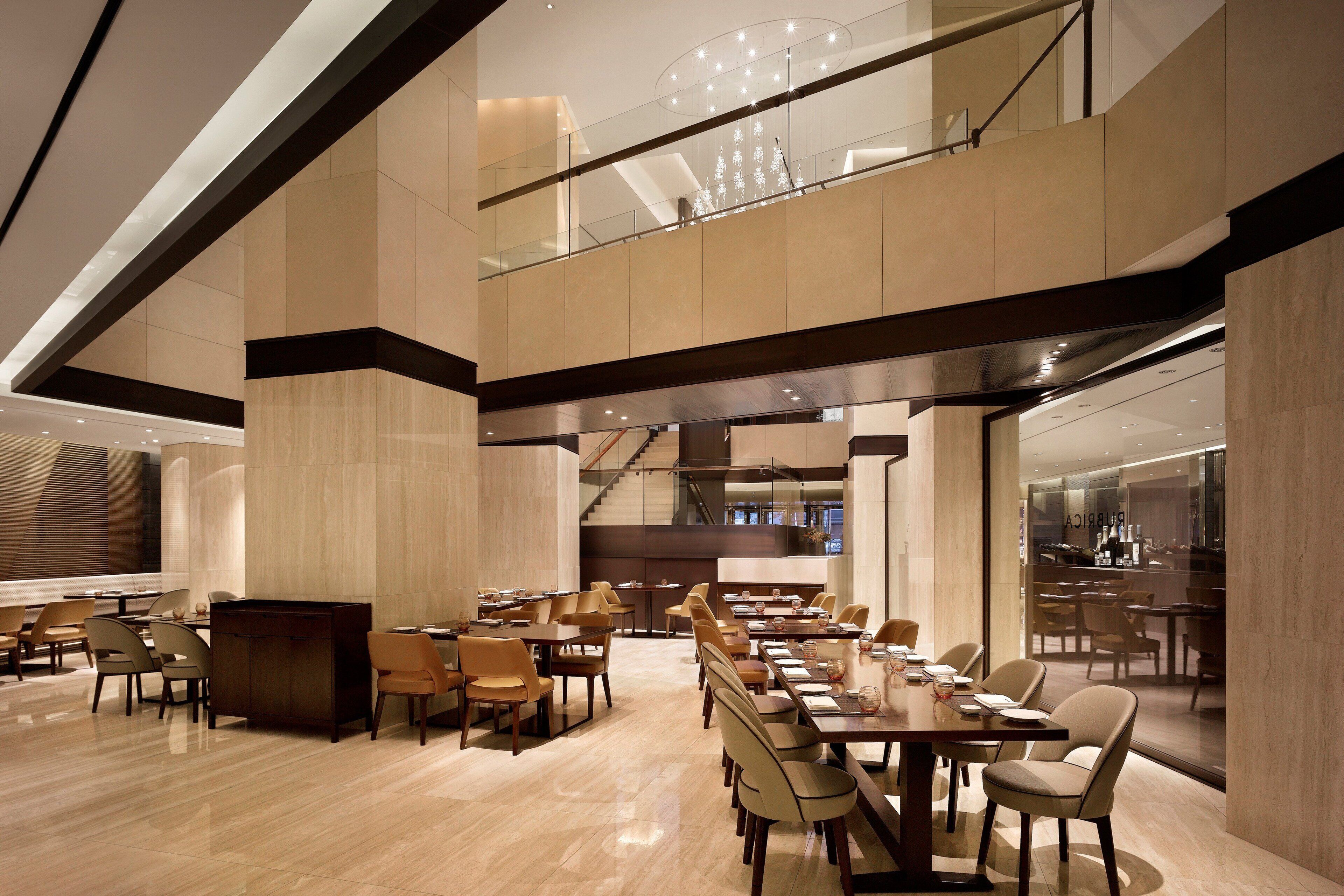 A spacious hotel lobby with multiple dining areas, a staircase, and a view of the bar area.