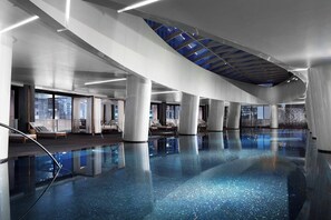 Une vaste piscine intérieure à l’eau d’un bleu limpide, dotée de grandes fenêtres et d’une architecture moderne.