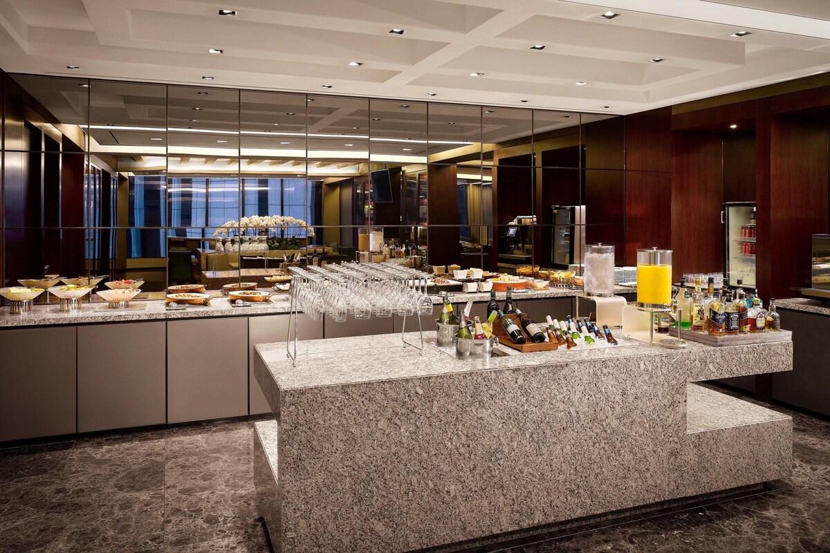 A modern hotel lobby with a marble reception desk, glassware, and a variety of beverages.