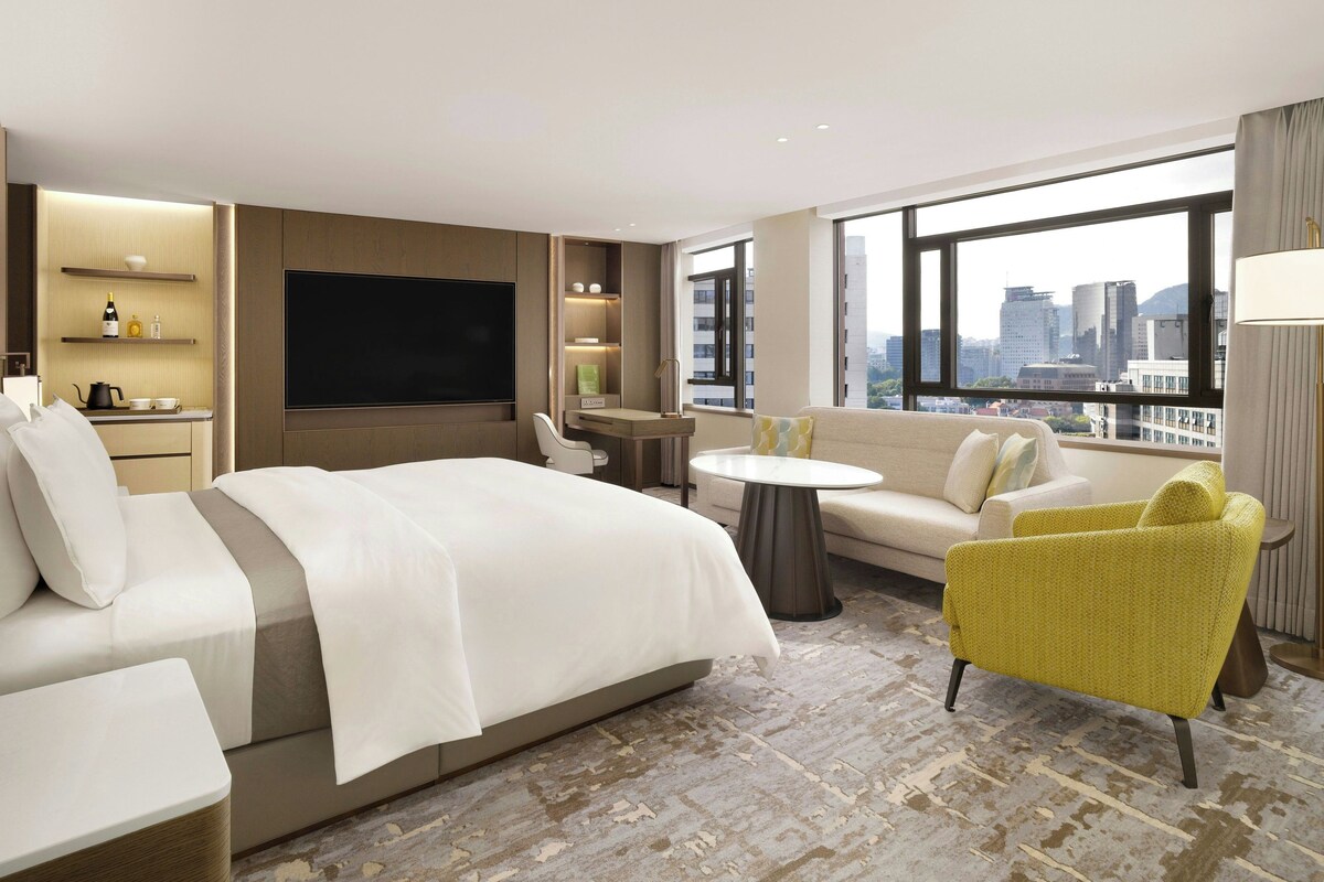 A modern hotel room with a large bed, a sofa, a small table, and a TV.