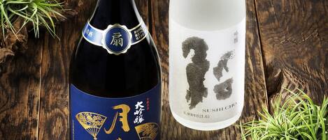 Two bottles of sake on a wooden surface with green plants.
