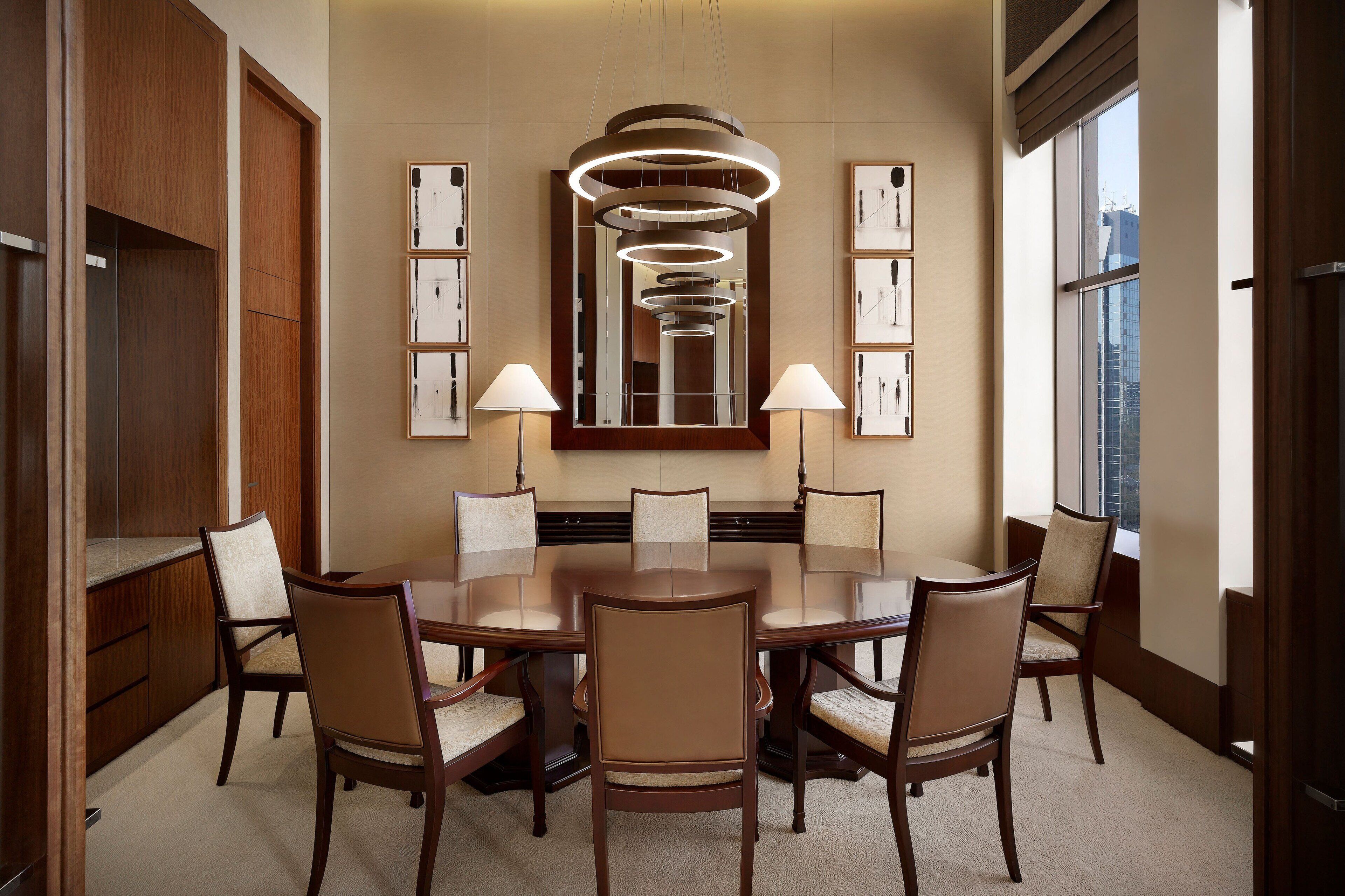 A conference room with a large oval table, six chairs, a modern chandelier, and framed artwork on the walls.