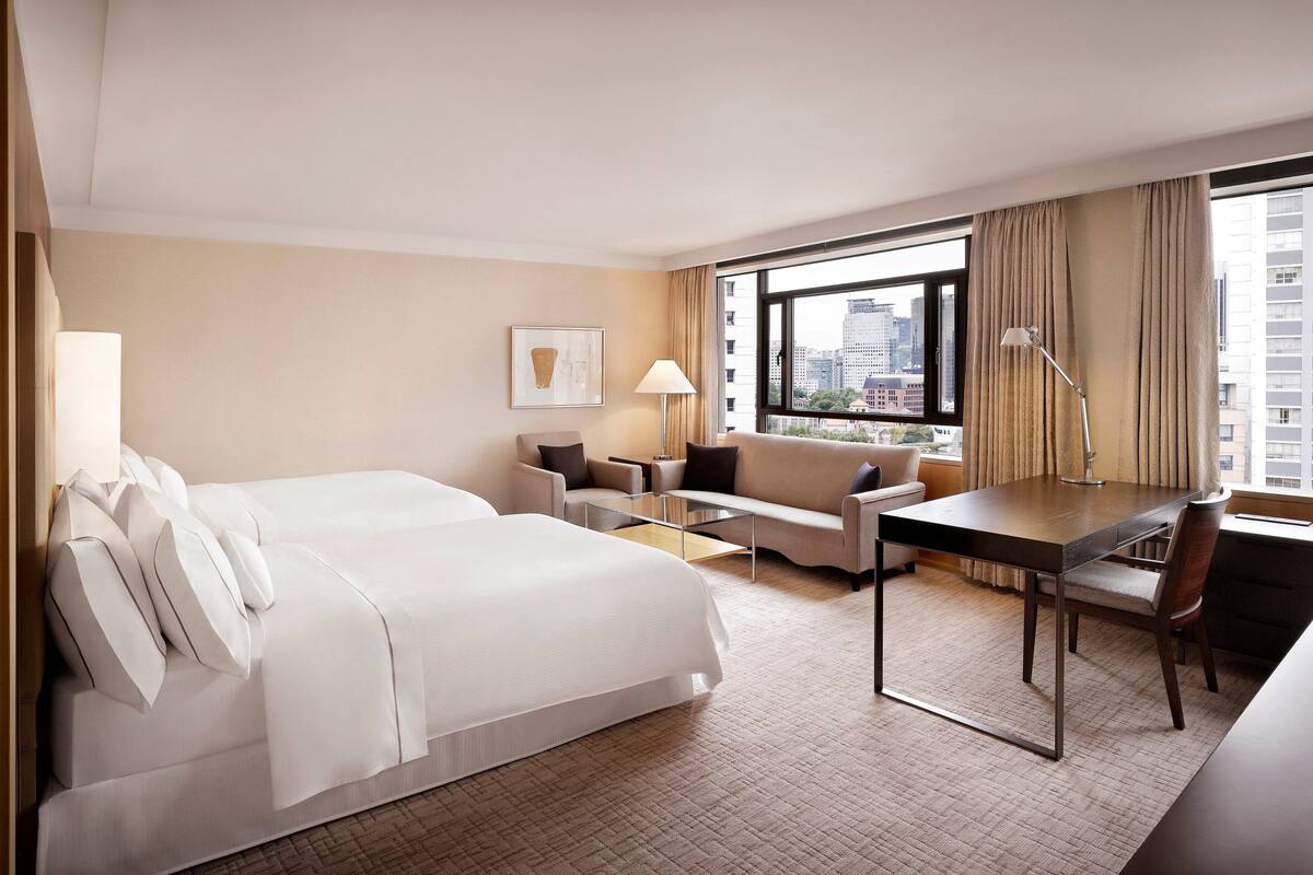 Een hotelkamer met een groot bed, een bank, een bureau en een raam met uitzicht op de stad.