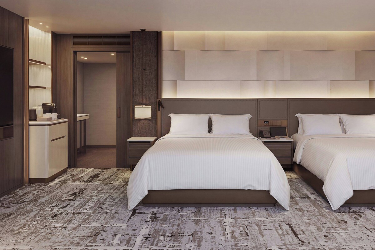 A hotel room with two beds, a bedside table, a nightstand, a desk, and a bathroom.