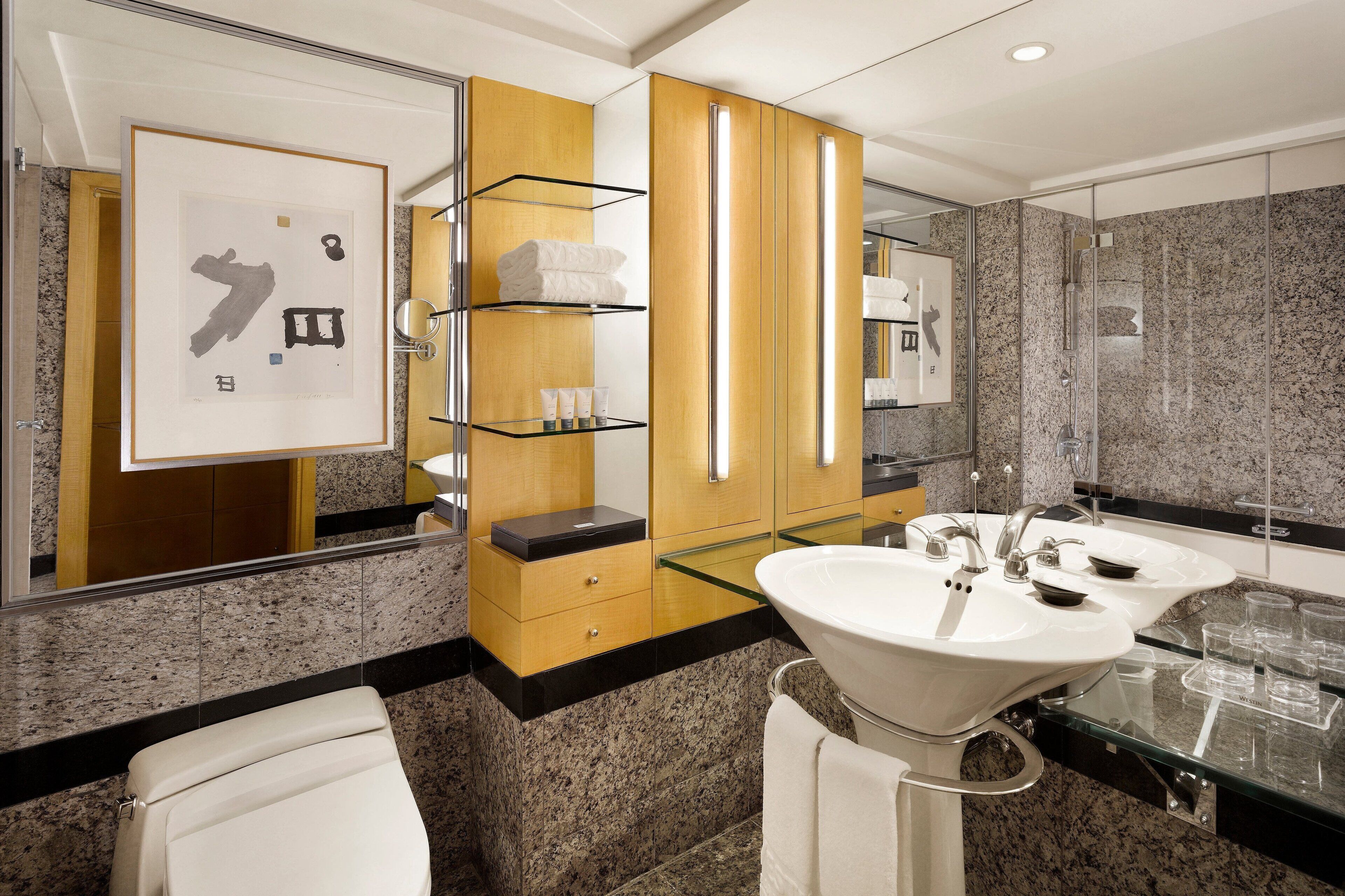 A modern bathroom with granite countertops, a large mirror, two sinks, and a glass shower enclosure.