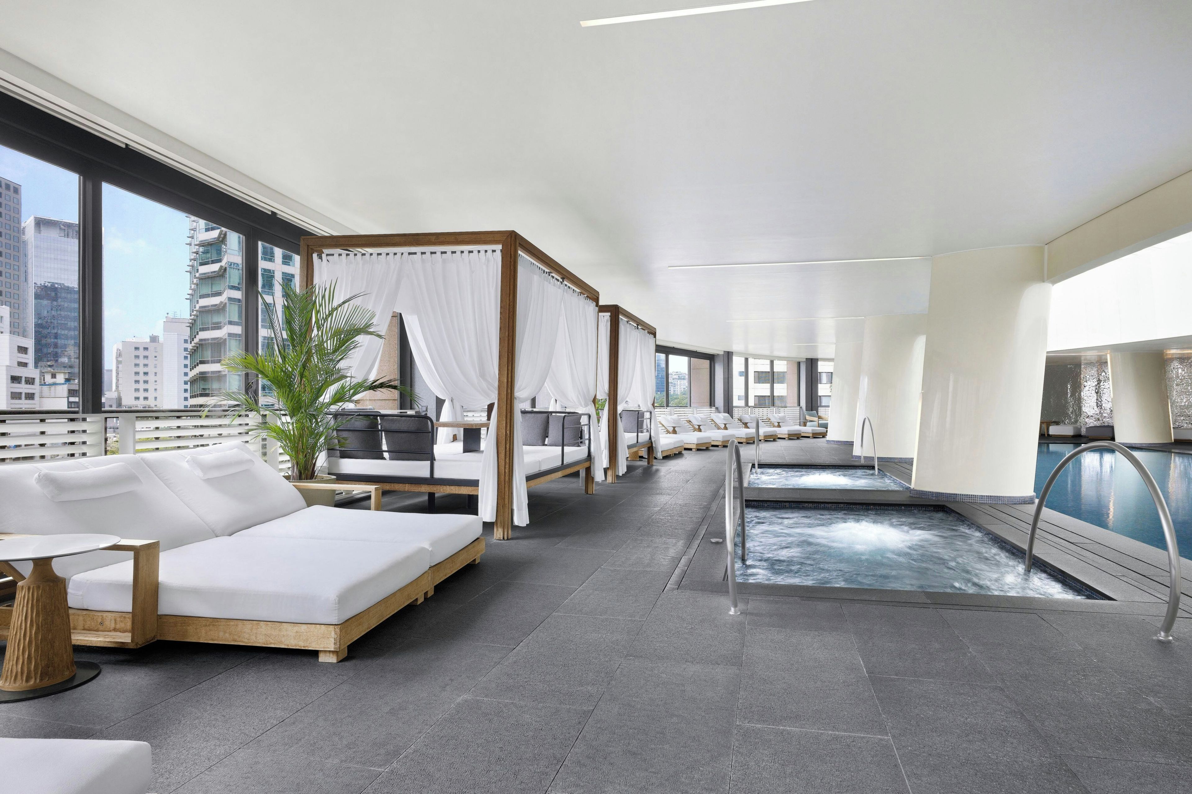 A modern hotel room with a large window, a private pool, and a balcony with a view of the city.