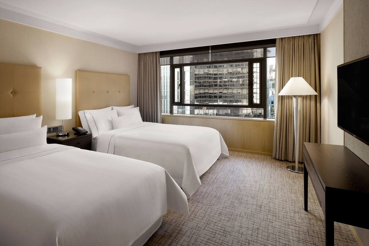 Een hotelkamer met twee bedden, een televisie, een lamp en een raam met gordijnen.