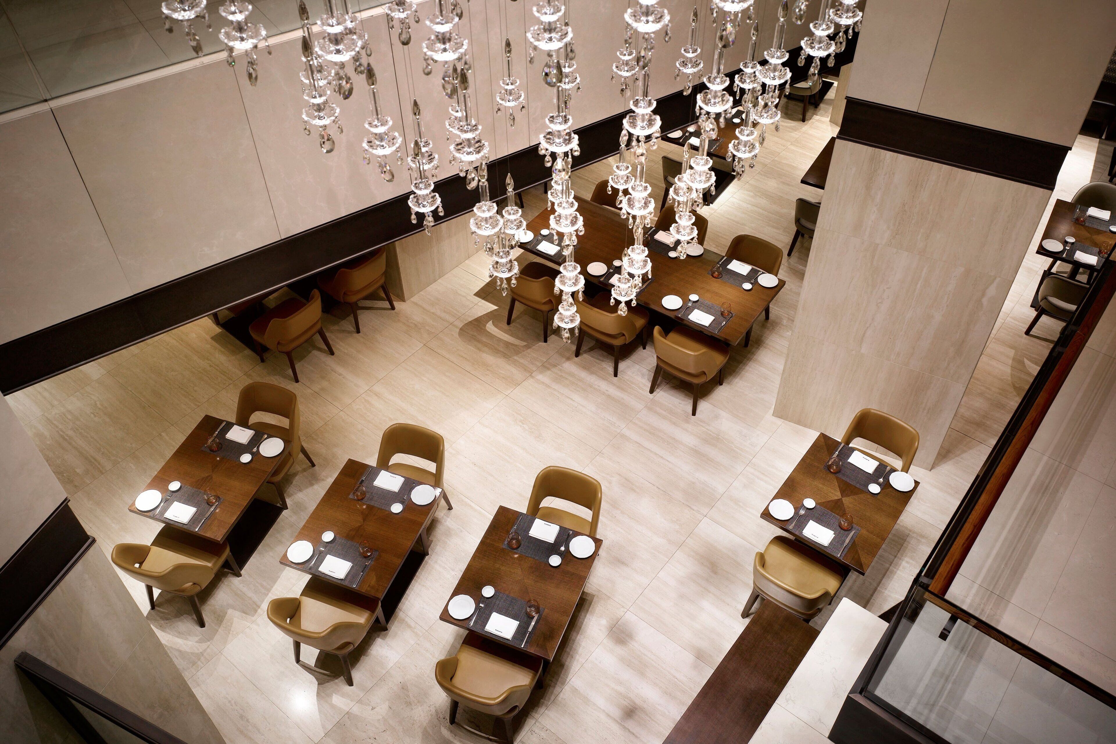 A modern hotel dining area with multiple tables and chairs, elegant chandeliers, and a clean, polished floor.