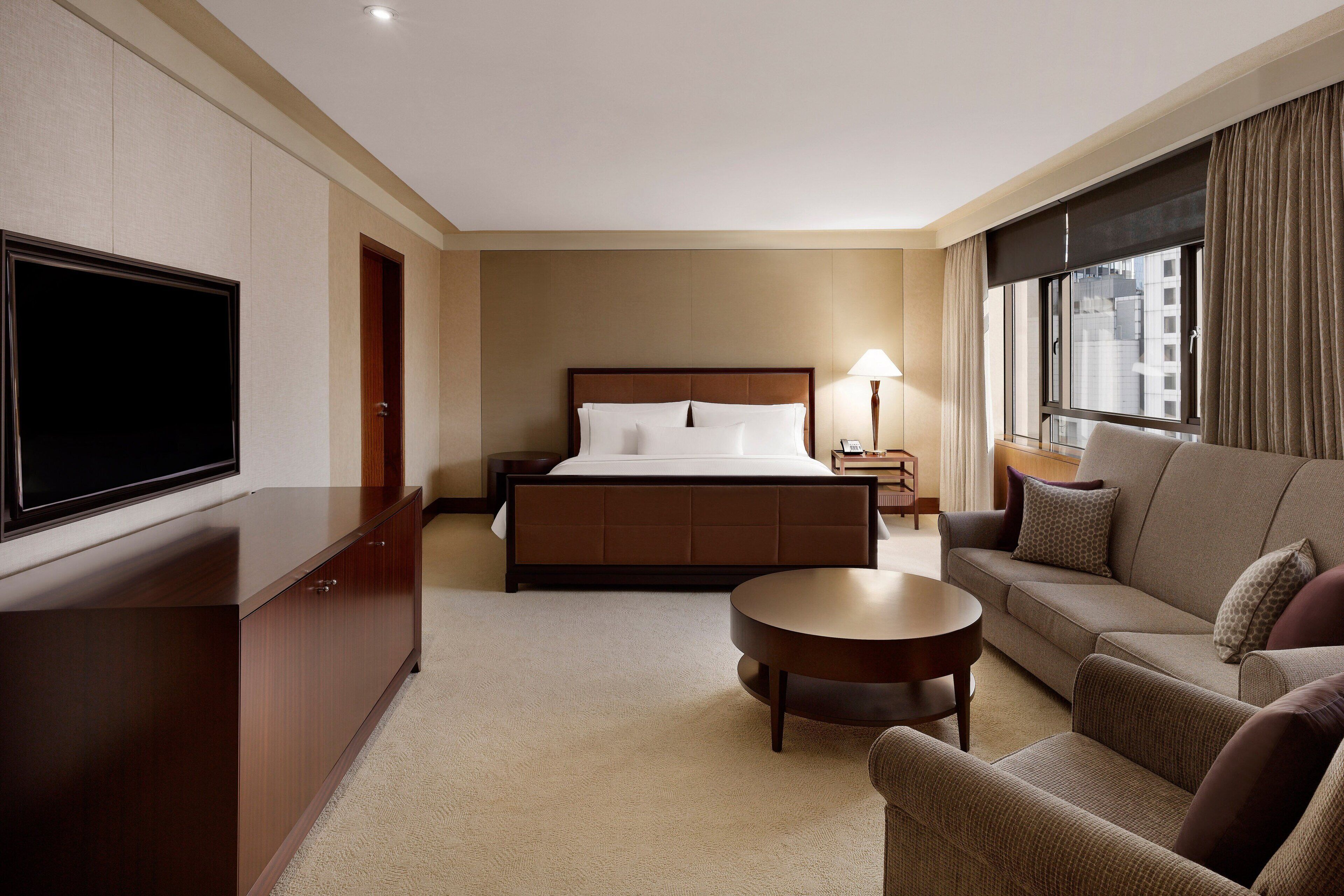 Ein Hotelzimmer mit einem großen Bett, einem Fernseher, einer Couch, einem Couchtisch und einem Fenster mit Vorhängen.