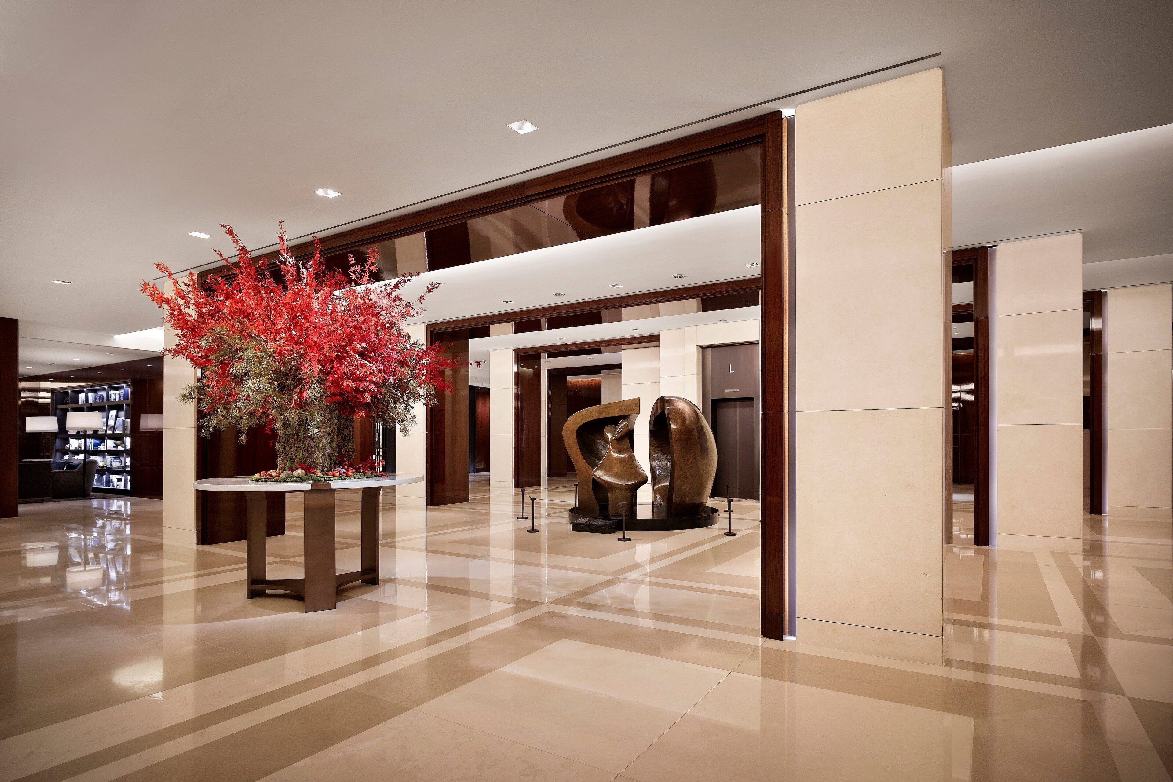 A spacious lobby with a polished floor, a large decorative plant, and a modern abstract sculpture.